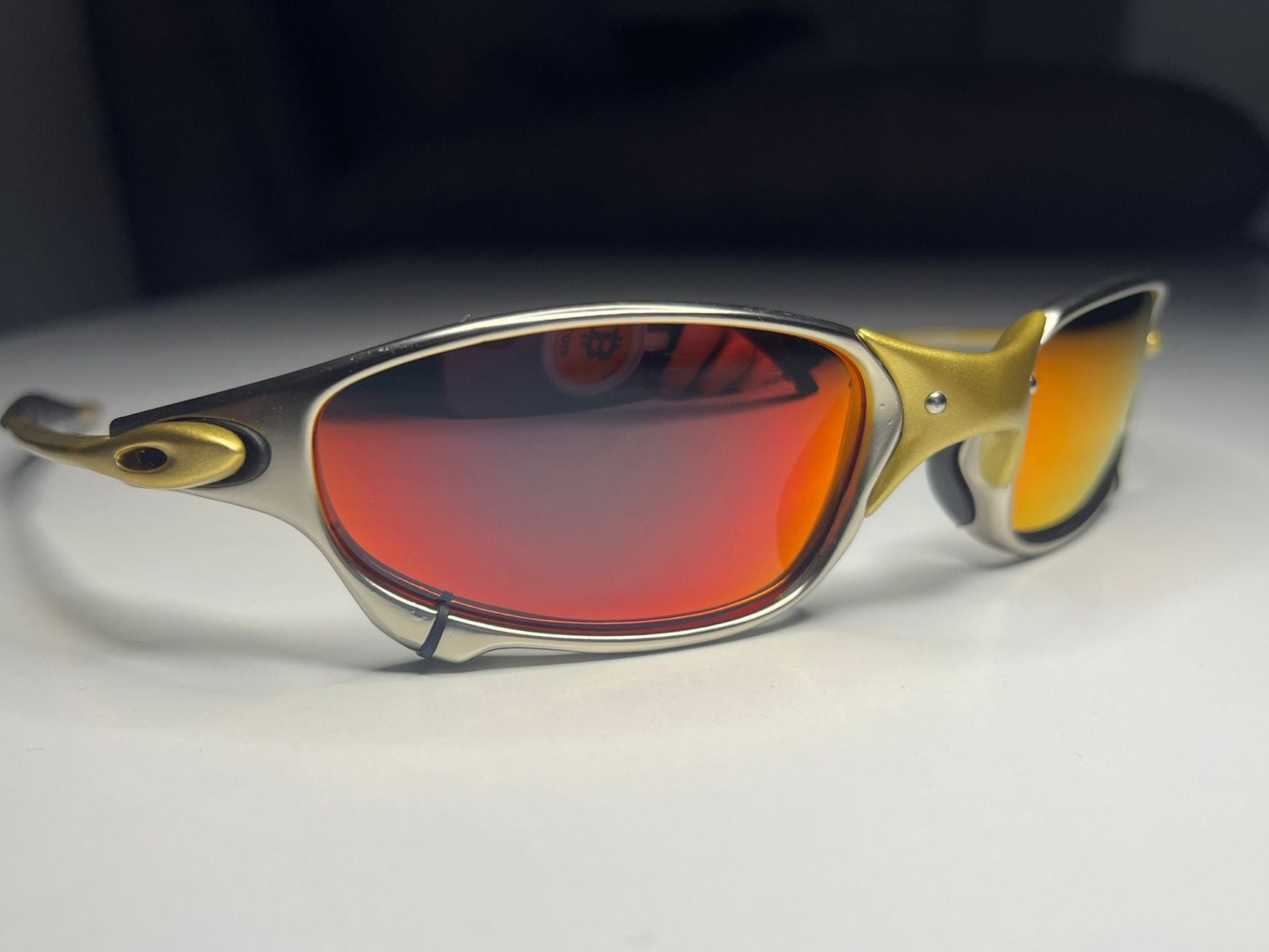 Gold-framed sunglasses with red lenses on a white surface