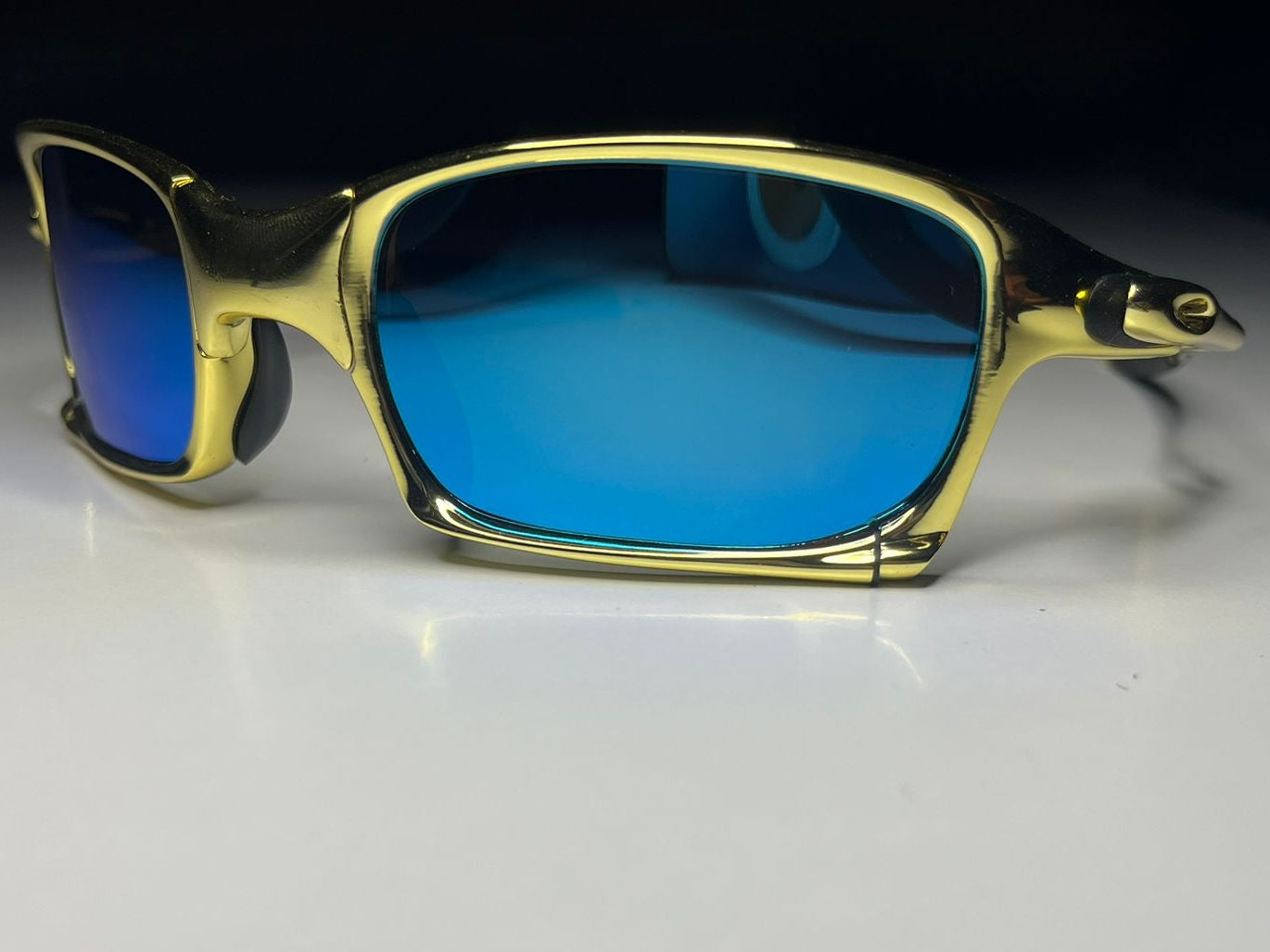 Gold-framed sunglasses with blue lenses on a white surface